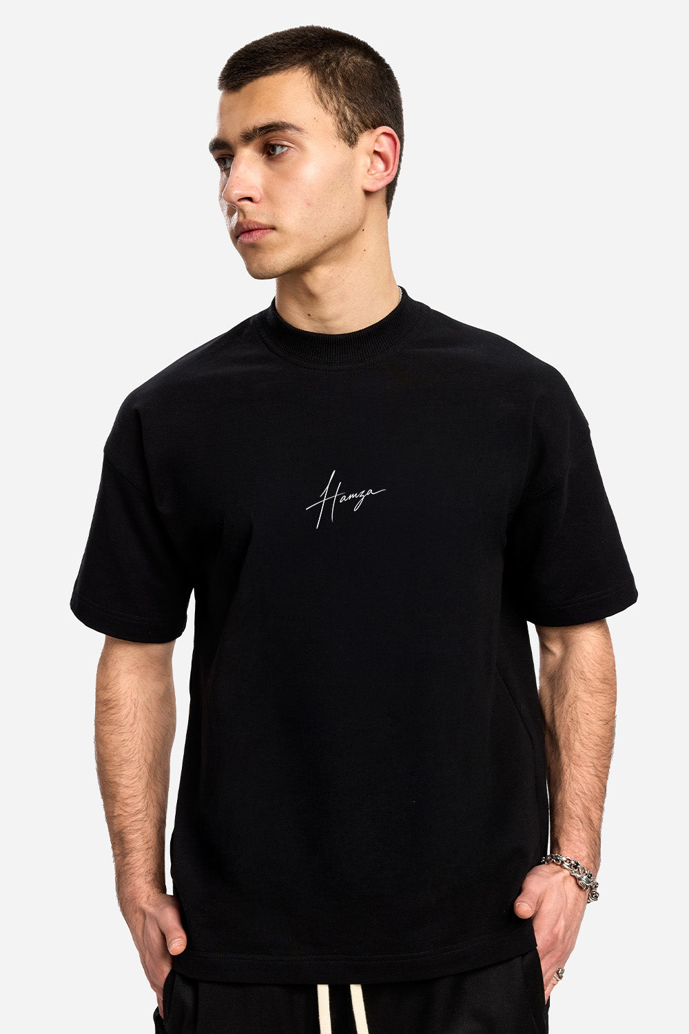 Vedere frontală din trei sferturi a unui model purtând tricoul oversized negru They Will Ignore You pentru bărbați, cu semnătura Hamza