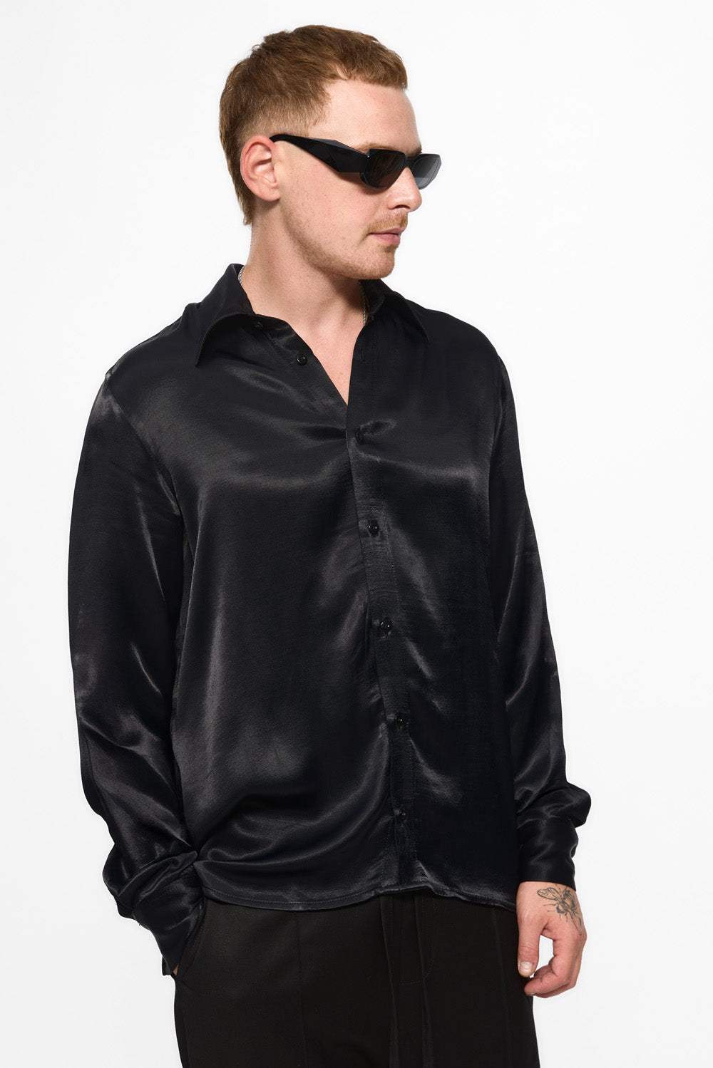 Person wearing a black satin shirt and sunglasses on a white background