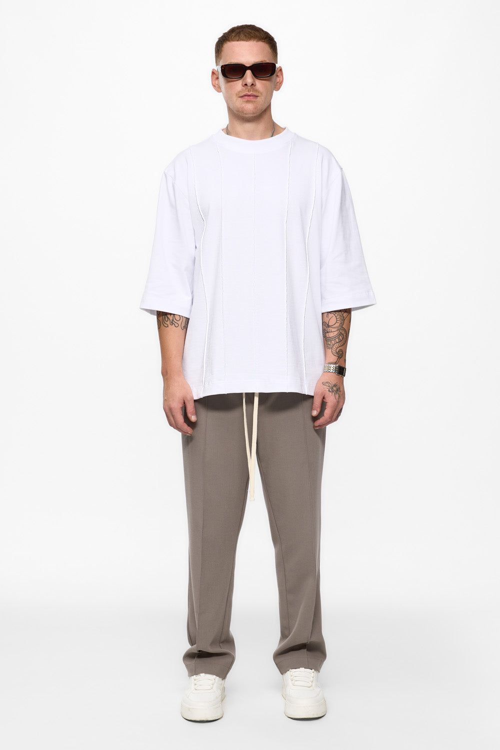 Man wearing a white oversized t-shirt, beige pants, and white sneakers on a white background