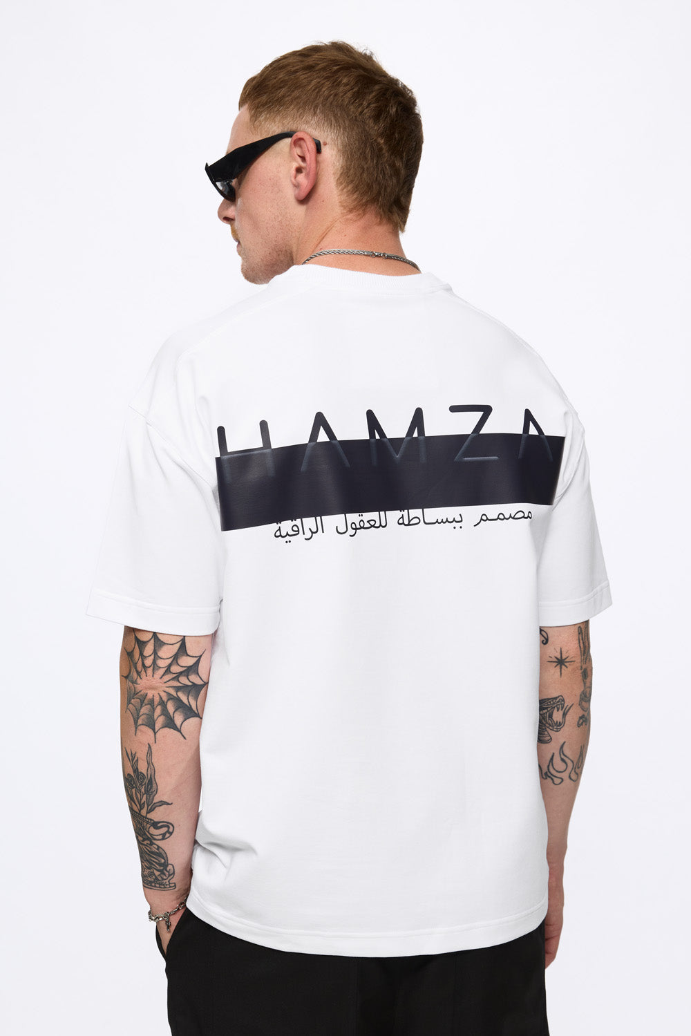 Person wearing a white t-shirt with black text and logo on the back, standing against a white background.