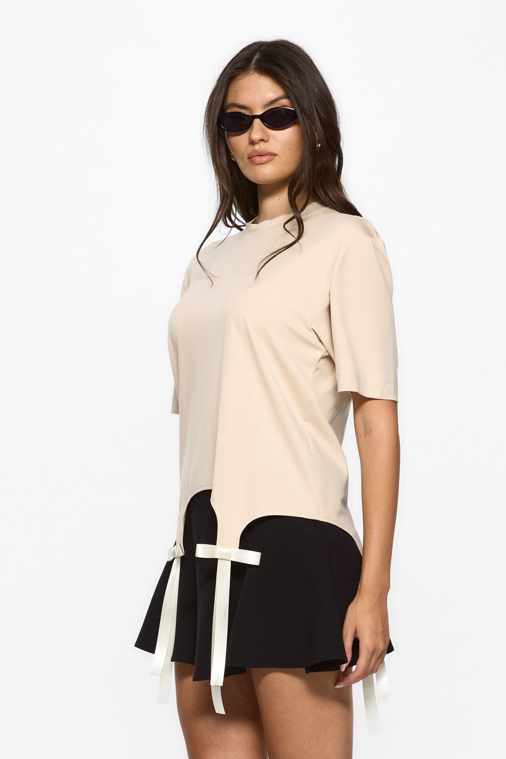 Woman wearing a beige top and black skirt with a white belt on a white background