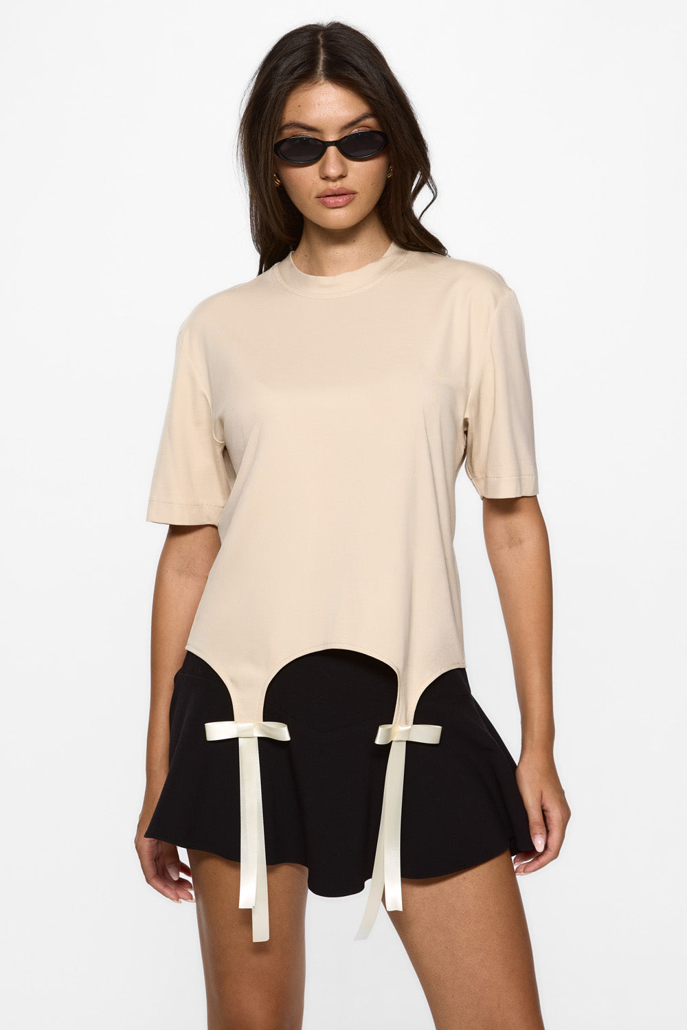 Woman wearing a beige top and black shorts with white ribbons on a white background