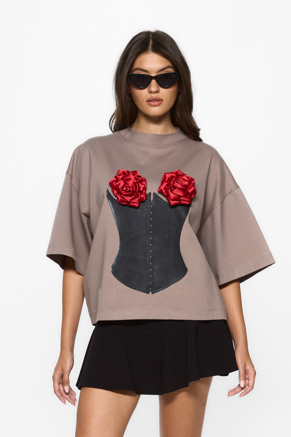 Woman wearing a beige oversized t-shirt with a corset design and red roses on a plain background