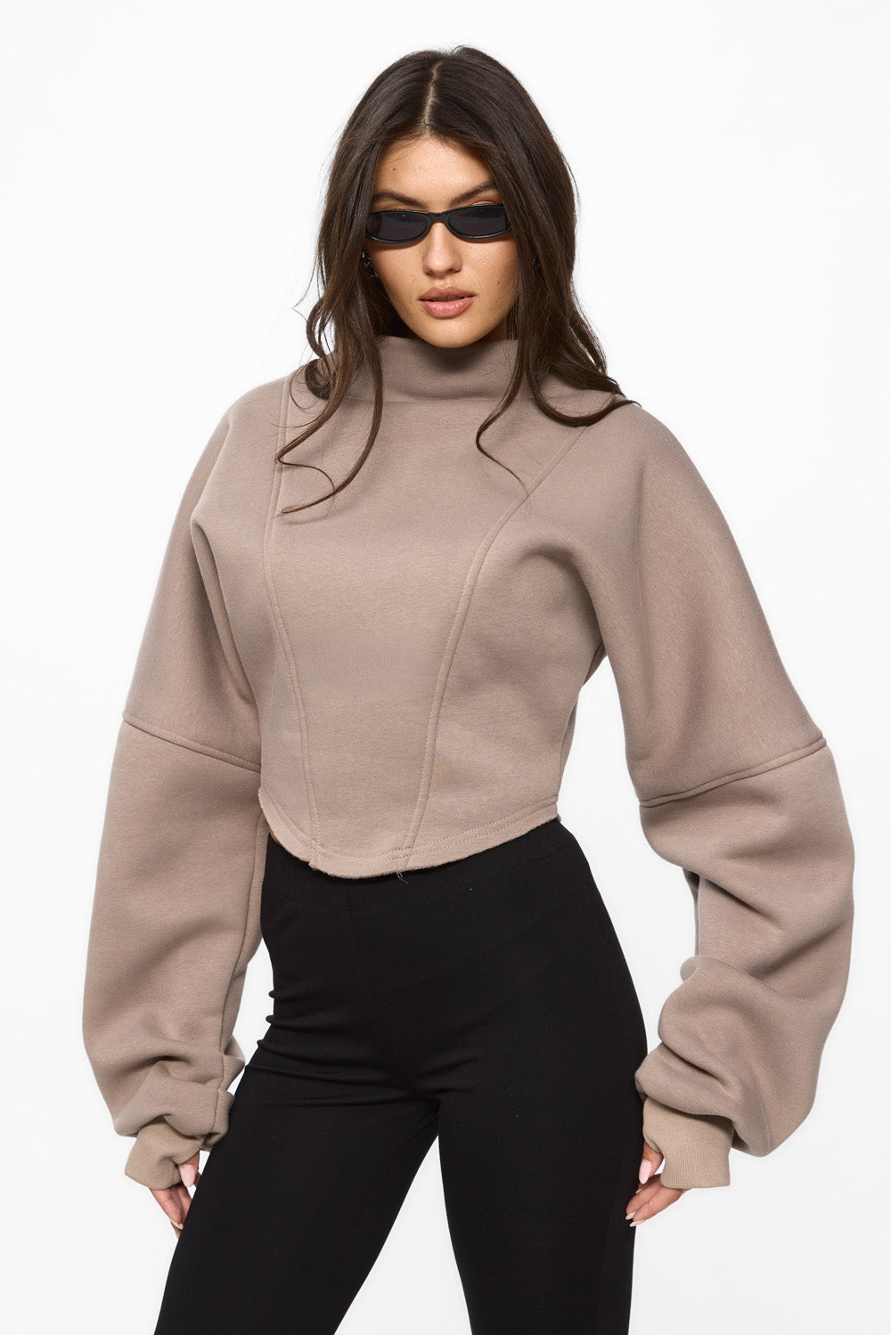 Woman wearing a beige cropped sweater and black pants on a white background